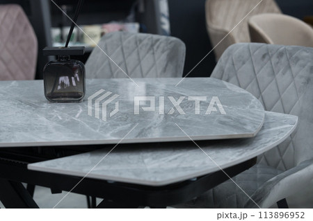 Gray wooden table complete with gray wooden chairs with soft fabric upholstery. Black glass jar with incense sticks on the table Gray wooden table complete with gray wooden chairs with soft fabric upholstery. Black glass jar with incense sticks on the table 113896952