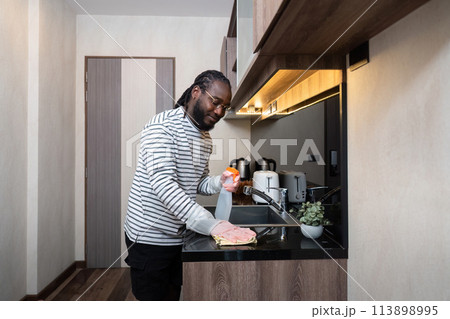 African American man in rubber gloves wipe dust from table in kitchen, Housework, cleaning, lifestyle, household African American man in rubber gloves wipe dust from table in kitchen, Housework, cleaning, lifestyle, household 113898995