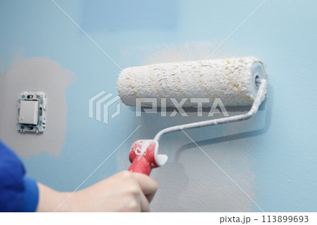 Close-up shot of a woman painting the wall of her house with a roller in a lighter color than the old one 113899693