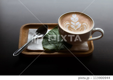 Hot latte coffee or Cappuccino with latte art in white coffee cup on wooden tray at wood background with light streaming from the window, adding to the enjoyment of coffee even more. Hot latte coffee or Cappuccino with latte art in white coffee cup on wooden tray at wood background with light streaming from the window, adding to the enjoyment of coffee even more. 113900944