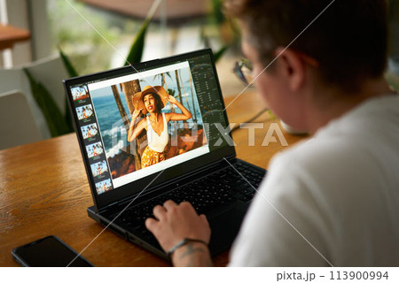 FTM photographer edits summer travel photo of model on laptop in cozy cafe, creative work. Over shoulder view, screen visible, freelance job, lifestyle. Multimedia, graphic design, photo editing. FTM photographer edits summer travel photo of model on laptop in cozy cafe, creative work. Over shoulder view, screen visible, freelance job, lifestyle. Multimedia, graphic design, photo editing. 113900994