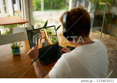 Gen Z pro in casual office setup participates in video call from home. Young person with headphones communicates online, discusses project with colleague. Modern work from anywhere concept. Gen Z pro in casual office setup participates in video call from home. Young person with headphones communicates online, discusses project with colleague. Modern work from anywhere concept. 113901011
