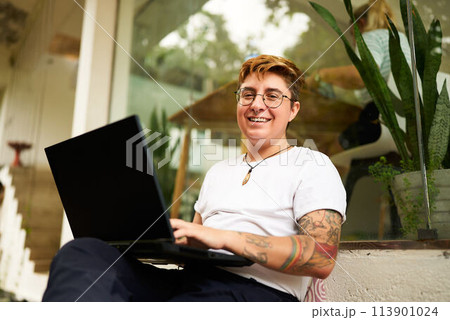 Transgender professional works on laptop, smiles in modern coworking space. Inclusive workplace, creative freelancing, comfy setting. Tattooed, gender diversity, productive remote working. Transgender professional works on laptop, smiles in modern coworking space. Inclusive workplace, creative freelancing, comfy setting. Tattooed, gender diversity, productive remote working. 113901024