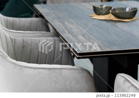 Gray wooden table combined with gray chairs with soft fabric upholstery. There is a black porcelain plate on the table Gray wooden table combined with gray chairs with soft fabric upholstery. There is a black porcelain plate on the table 113902249