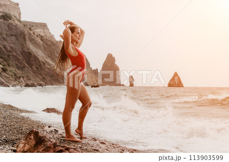 Woman summer travel sea. Happy tourist in red bikini enjoy taking picture outdoors for memories. Woman traveler posing on beach at sea surrounded by volcanic mountains, sharing travel adventure joy Woman summer travel sea. Happy tourist in red bikini enjoy taking picture outdoors for memories. Woman traveler posing on beach at sea surrounded by volcanic mountains, sharing travel adventure joy 113903599
