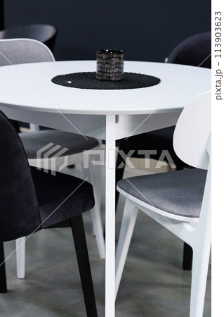 White wooden table combined with black and white wooden chairs with soft fabric upholstery. There is a black wax candle on the table 113903623