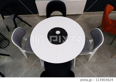 White wooden table combined with black and white wooden chairs with soft fabric upholstery. There is a black wax candle on the table 113903624