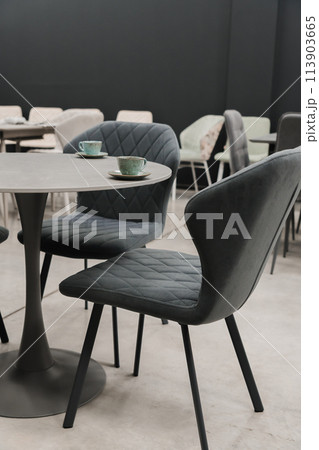 Gray wooden table combined with dark gray wooden chairs with soft fabric upholstery. There are blue porcelain mugs and saucers on the table 113903665