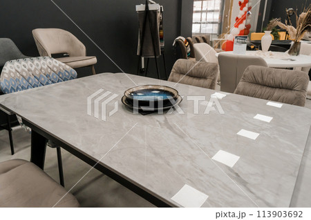 Gray wooden table combined with beige wooden chairs with soft fabric upholstery. Blue and black porcelain plates on the table Gray wooden table combined with beige wooden chairs with soft fabric upholstery. Blue and black porcelain plates on the table 113903692