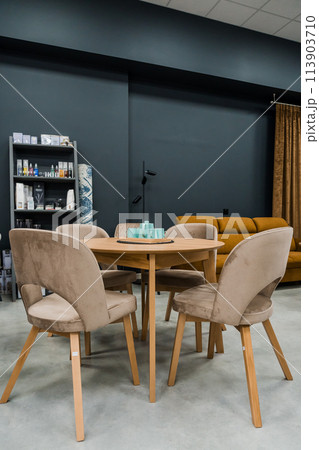 A yellow wooden table combined with beige wooden chairs with soft fabric upholstery. There is a porcelain teapot and blue mugs on the table 113903710