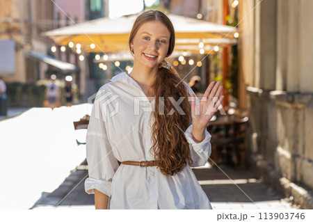 Young girl smiling friendly at camera, waving hands hello, hi, greeting or goodbye in city street Young girl smiling friendly at camera, waving hands hello, hi, greeting or goodbye in city street 113903746