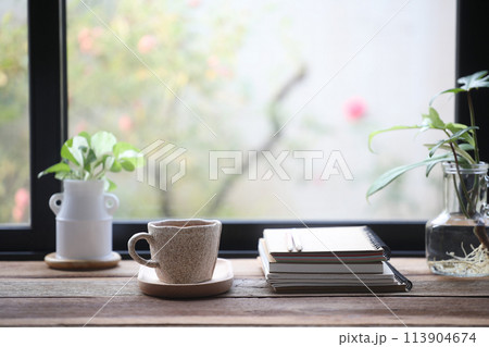 Coffee in a white cup and notebooks on wooden table with plants 113904674