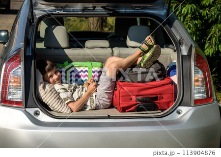 Cute little boy laying on the back of the bags and baggage in the car trunk ready to go on vacation with happy expression. Kid resting playing on smartphone Cute little boy laying on the back of the bags and baggage in the car trunk ready to go on vacation with happy expression. Kid resting playing on smartphone 113904876