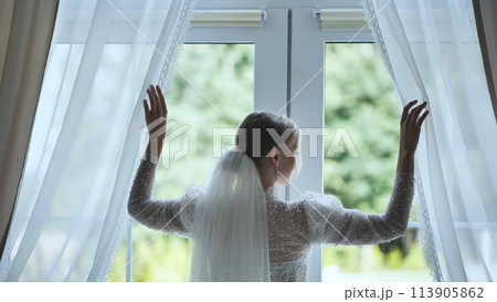 The bride adjusts the curtains at the window. 113905862