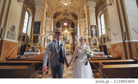 The bride and groom walk through a Catholic church. 113905869