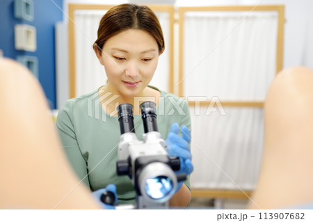Gynecologist examines a patient using microscope in a gynecological chair. Doctor performs a colposcopy on a young girl in a modern medical office. Diagnosis of cervical cancer. Gynecologist examines a patient using microscope in a gynecological chair. Doctor performs a colposcopy on a young girl in a modern medical office. Diagnosis of cervical cancer. 113907682