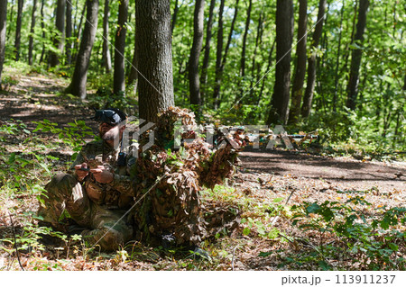 A skilled sniper and a soldier operating a drone with VR goggles strategize and observe the military action while concealed in the forest 113911237