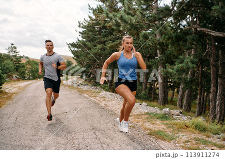 A couple dressed in sportswear runs along a scenic road during an early morning workout, enjoying the fresh air and maintaining a healthy lifestyle A couple dressed in sportswear runs along a scenic road during an early morning workout, enjoying the fresh air and maintaining a healthy lifestyle 113911274