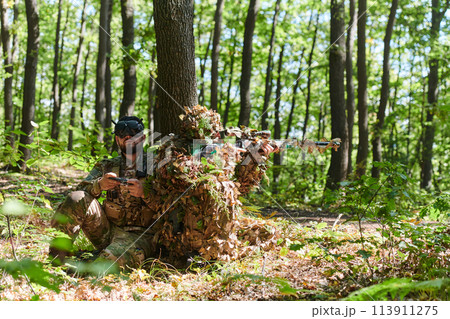 A skilled sniper and a soldier operating a drone with VR goggles strategize and observe the military action while concealed in the forest A skilled sniper and a soldier operating a drone with VR goggles strategize and observe the military action while concealed in the forest 113911275