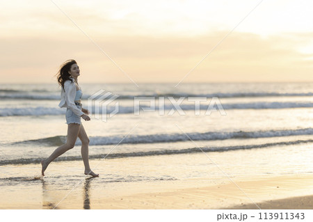 A woman is running on the beach at sunset A woman is running on the beach at sunset 113911343