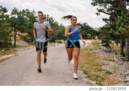 A couple dressed in sportswear runs along a scenic road during an early morning workout, enjoying the fresh air and maintaining a healthy lifestyle 113911659