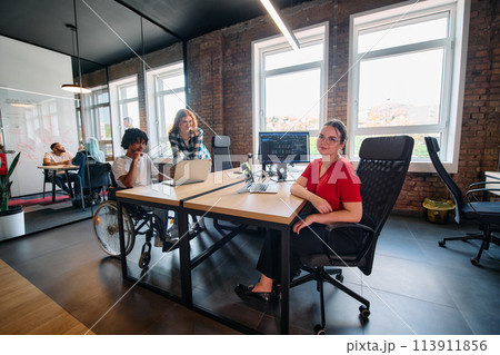 A diverse group of business professionals collaborates in a modern startup coworking center, utilizing a mix of paper-based and technological tools such as mobile phones and computers  113911856