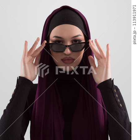 Portrait of beautiful stylish young muslim woman wearing black hijab and sunglasses as modern eastern fashion concept posing on white background. Portrait of beautiful stylish young muslim woman wearing black hijab and sunglasses as modern eastern fashion concept posing on white background. 113911971