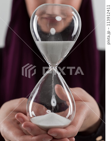 Beautiful arab businesswoman wearing hijab and holding sand clock. Time is passing and it's a pressure concept. 113912411