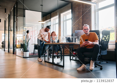 A diverse group of business professionals collaborates in a modern startup coworking center, utilizing a mix of paper-based and technological tools such as mobile phones and computers  113912837