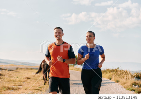 A couple dressed in sportswear runs along a scenic road during an early morning workout, enjoying the fresh air and maintaining a healthy lifestyle 113913149