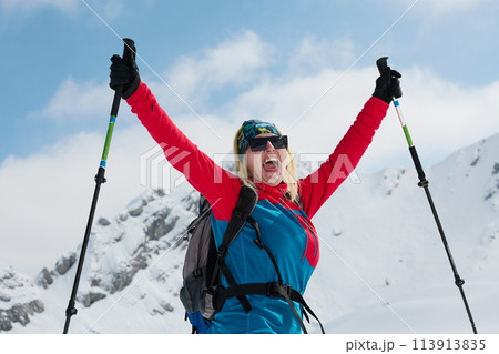 A professional woman skier rejoices after successfully climbing the snowy peaks of the Alps 113913835