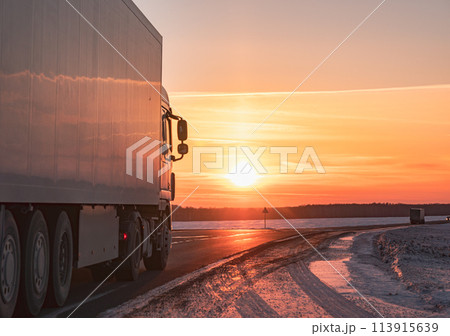Semi truck driving along a snowy highway at sunset in winter Semi truck driving along a snowy highway at sunset in winter 113915639