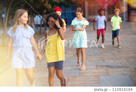 Two cheerful preteen girls enjoying walk along city street 113918184