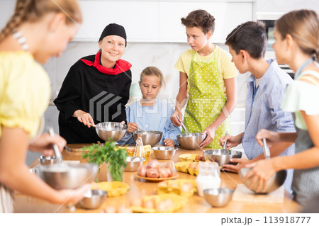 Friendly female chef in black uniform giving culinary lesson to tweens Friendly female chef in black uniform giving culinary lesson to tweens 113918777