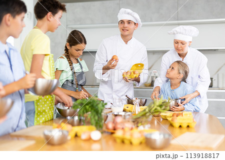 Positive professional chefs in white uniform conducting culinary masterclass for tweens Positive professional chefs in white uniform conducting culinary masterclass for tweens 113918817