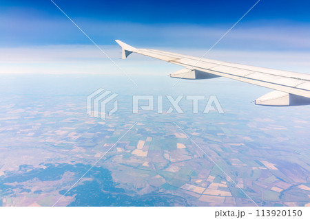 Aerial view from airplane window above green ground. View from the airplane window with beautiful clouds at sunrise Aerial view from airplane window above green ground. View from the airplane window with beautiful clouds at sunrise 113920150
