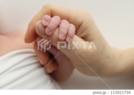 Close-up little hand of child and palm of mother and father. The newborn baby has a firm grip on the parent's finger after birth. A newborn holds on to mom's, dad's finger. 113921756