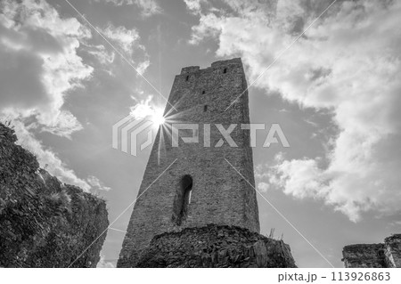 The sun casts a radiant burst of light beside the towering remains of Okor Castle close to Prague, captured in striking monochromatic tones. Czechia. Black and white photography. The sun casts a radiant burst of light beside the towering remains of Okor Castle close to Prague, captured in striking monochromatic tones. Czechia. Black and white photography. 113926863