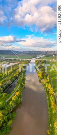 An aerial view of the Lahovice Bridge spanning the Berounka River, surrounded by lush greenery under a cloudy sky. Prague, Czechia 113926900