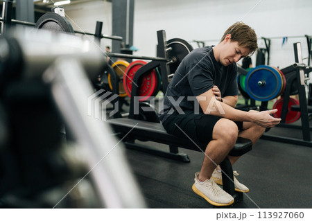 Side view of sportsman having accident injury and hurt at arms while workout with barbell weight training at gym. Athletic man suffering from muscle injury exercising at sport club. Side view of sportsman having accident injury and hurt at arms while workout with barbell weight training at gym. Athletic man suffering from muscle injury exercising at sport club. 113927060