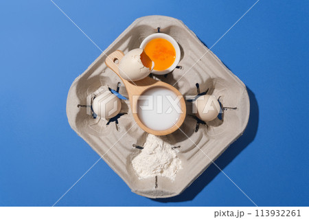 Dark blue background against a set of ingredients for homemade baking, flat lay with eggs, flour, nuts and milk. Top view with copy space for adding text 113932261