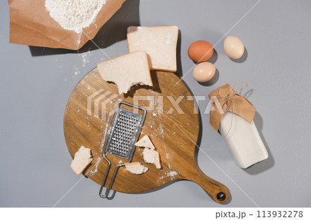 Creative flat lay photo of cooking concept with a wooden chopping board in center contained a metal zester and sandwich pieces decorated by some eggs. Top view photo with blank space for design Creative flat lay photo of cooking concept with a wooden chopping board in center contained a metal zester and sandwich pieces decorated by some eggs. Top view photo with blank space for design 113932278