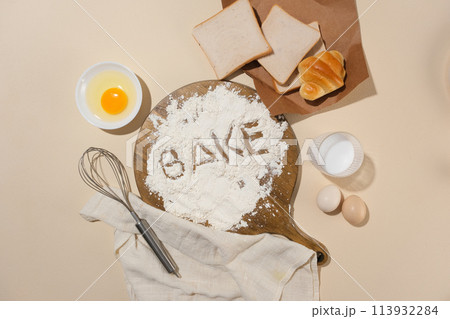 Round wooden chopping board sprinkled by flour lay flat on pink kitchen counter top, surrounded by other ingredients and utensils of baking. Top view with blank space for displaying product Round wooden chopping board sprinkled by flour lay flat on pink kitchen counter top, surrounded by other ingredients and utensils of baking. Top view with blank space for displaying product 113932284