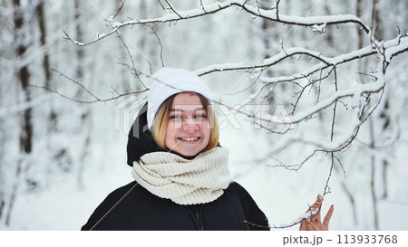 A girl gently touches snowy tree branches in the forest. 113933768
