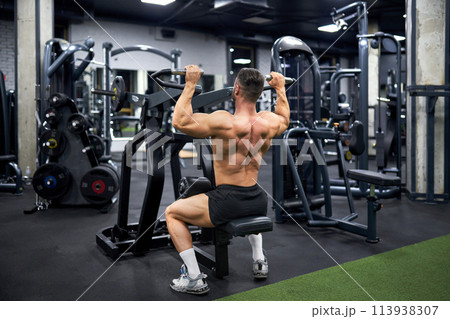 Attractive muscular man doing exercise with training apparatus in sports gym. Back view of strong unrecognizable male athlete with bare torso, building muscles indoors. Sport, bodybuilding concept. 113938307