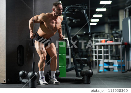 Focused sportsman bending body, while exercising on training apparatus. Full length of muscular male athlete doing pull-downs, lifting weights of cable training apparatus in gym. Crossfit concept. 113938360