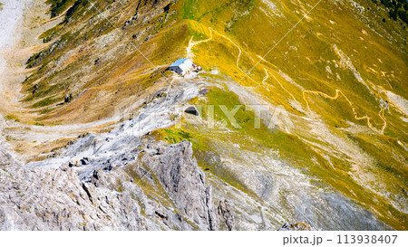 A high-angle view of the Tabaretta hut perched on the slopes of Ortles mountain, surrounded by meandering trails and green alpine terrain, showcasing the serene landscape of Italy diverse geography. 113938407