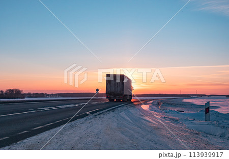 Semi truck driving along a snowy highway at sunset in winter 113939917