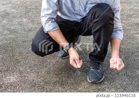 A man is kneeling on the ground and looking at his watch A man is kneeling on the ground and looking at his watch 113940118