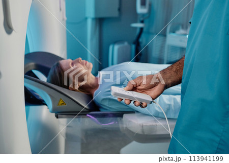 Unrecognizable radiographer holding controller turning on MRI scanner for mature Caucasian female patient, copy space 113941199
